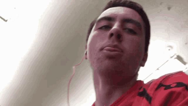 a man wearing headphones and a red shirt with the letter a on it looks at the camera