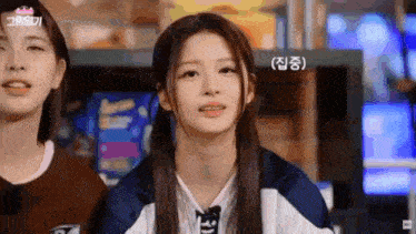 two girls are sitting next to each other in a room and one of them is looking at the camera .