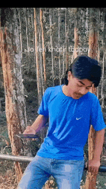 a man in a blue shirt is leaning against a tree looking at his phone