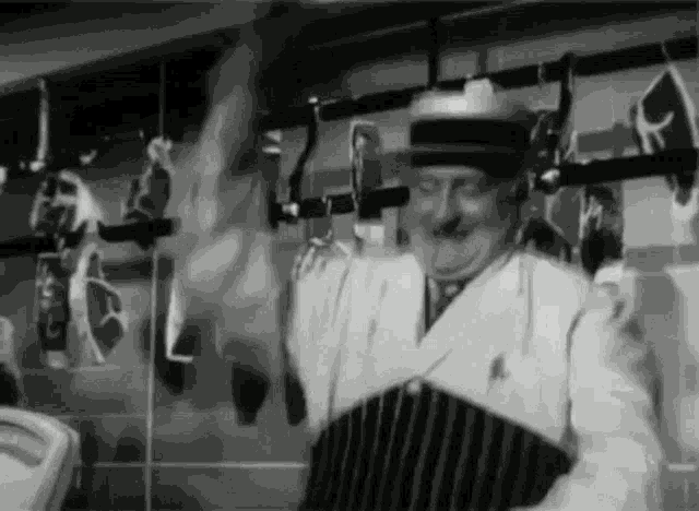 a black and white photo of a butcher holding a piece of meat in a butcher shop .