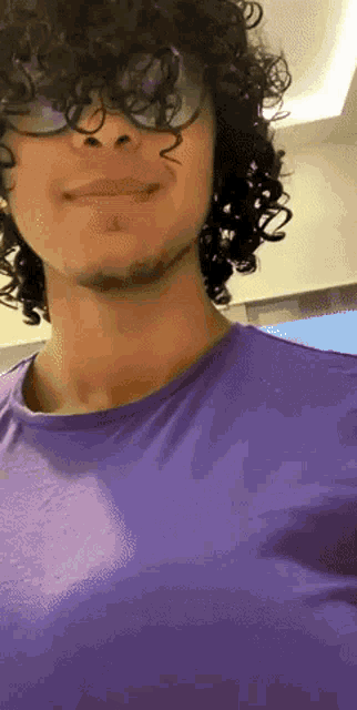 a man with curly hair wearing a purple shirt and glasses