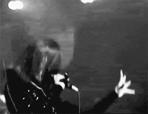 a black and white photo of a woman singing into a microphone while making a hand gesture .