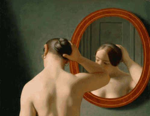 a man adjusts his hair in front of a mirror