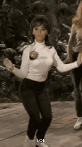 a woman in a white turtleneck and black pants is dancing with a group of people .