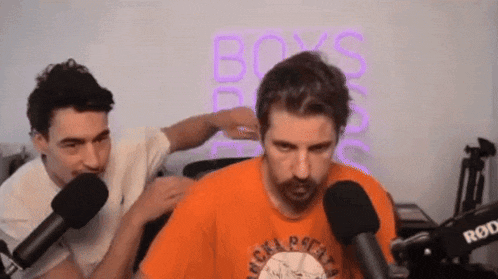 two men are talking into microphones in front of a neon sign that says boys on it .