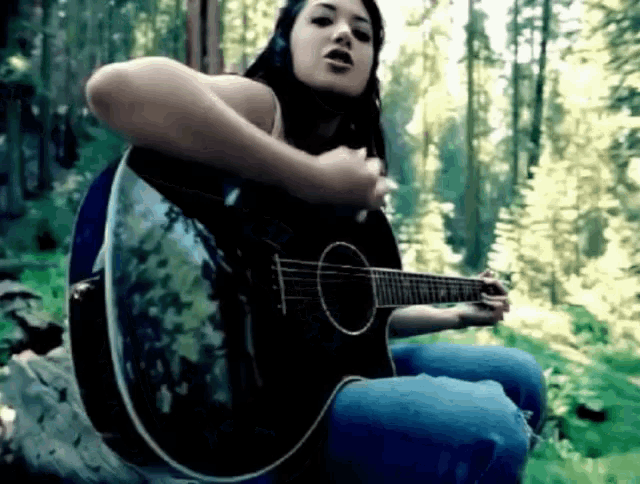 a woman playing a guitar in the woods with trees in the background