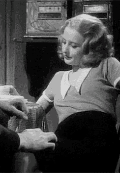 a black and white photo of a woman sitting in a chair with a man 's hand on her waist .
