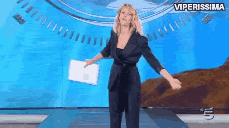 a woman in a black suit is standing on a stage with her arms outstretched and a sign that says viperissima above her