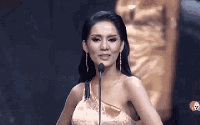 a woman in a gold dress is talking into a microphone .
