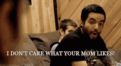 a man with a beard is sitting on a couch and says i don t care what your mom likes