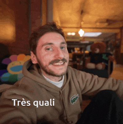 a man wearing a brown hoodie with the word très quali on the bottom