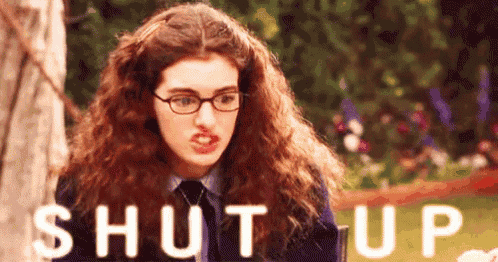 a woman with curly hair and glasses is making a funny face and the words shut up are behind her .