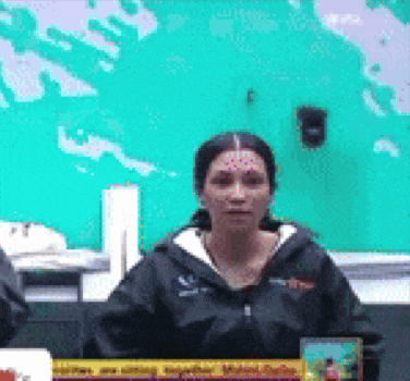 a woman in a black jacket sitting at a table with a sign that says ' a ' on it