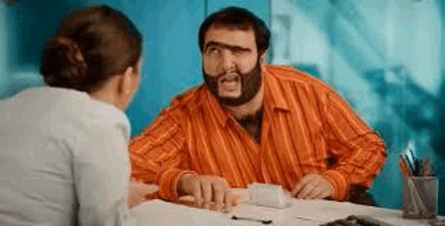 a man with a beard is sitting at a table with a woman and talking to her .