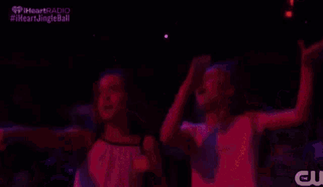 two girls are dancing in a dark room with a purple light behind them .