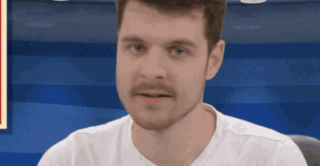 a man with a beard wearing a white shirt is looking at the camera