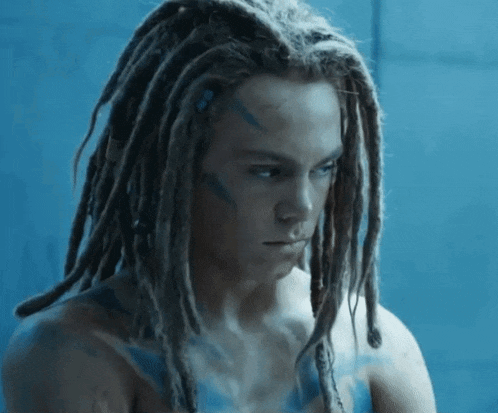 a man with dreadlocks and blue paint on his face looks down