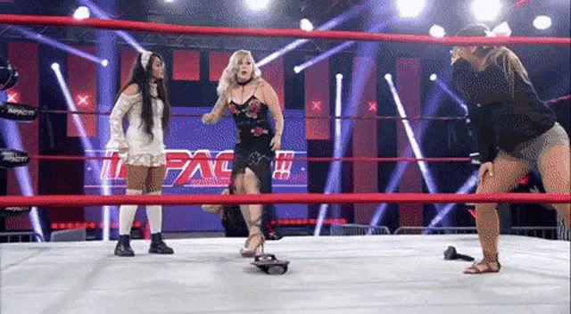 three women are standing in a wrestling ring with the word impact on the wall behind them