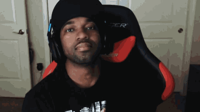 a man wearing a black hat and headphones sits in a red and black chair with the word cer on it
