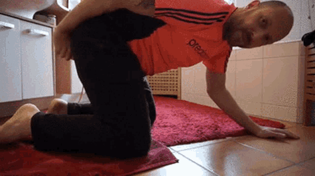 a man wearing an orange adidas shirt is kneeling on a red rug