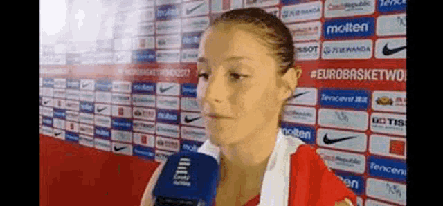 a woman is talking into a microphone in front of a wall with logos for nike and molten .