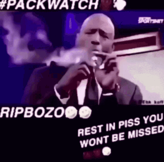 a man in a suit and tie is smoking a cigarette and talking into a microphone .