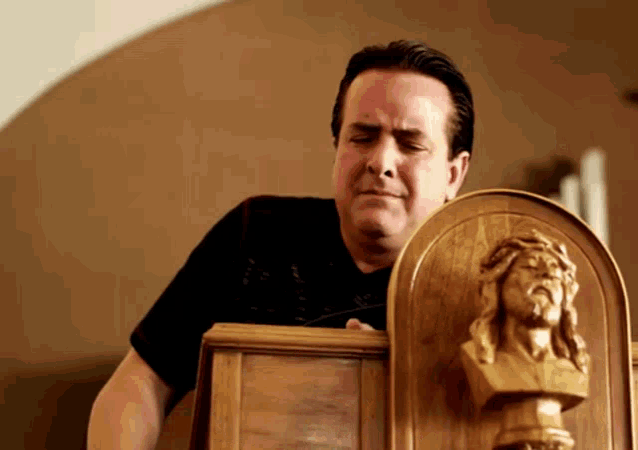 a man in a black shirt holds a wooden plaque with a jesus statue on it