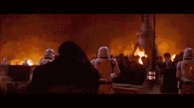 a person in a mask is holding a red light saber in front of a crowd of stormtroopers .