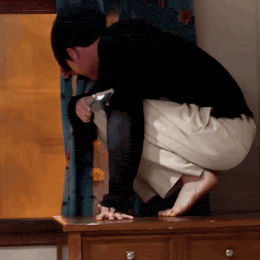 a man is kneeling down on a wooden dresser looking through a magnifying glass