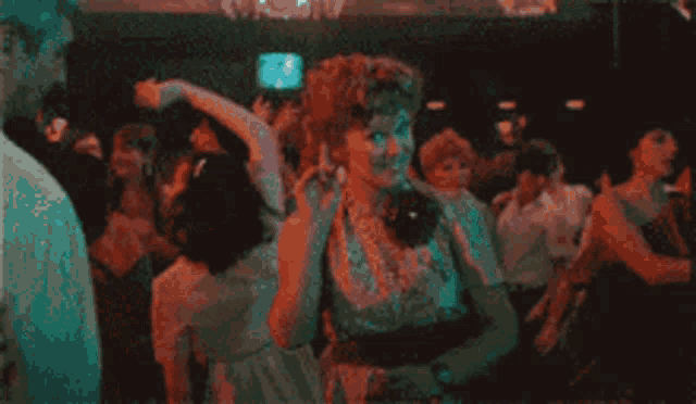 a man in a white shirt is dancing in a dark room with a crowd behind him .
