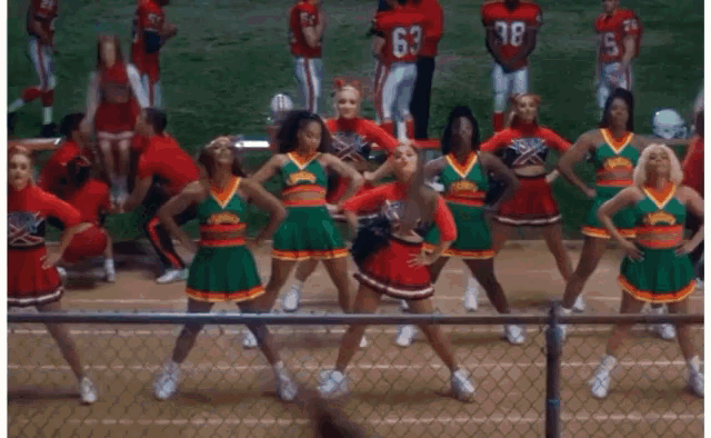 a group of cheerleaders are dancing on a field and one of them is wearing a red uniform .