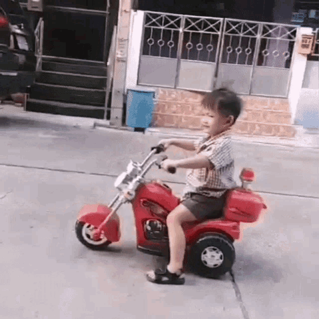 a little boy is riding a red toy motorcycle on the sidewalk .
