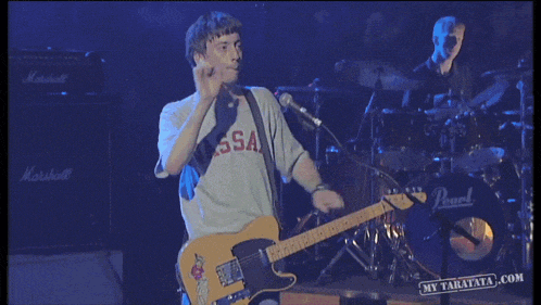 a man wearing a vassa shirt playing a guitar