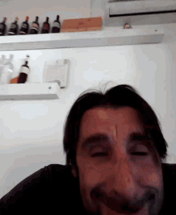a man is smiling in front of a shelf of bottles