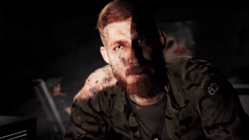 a man in a military uniform with a beard is standing in the dark .