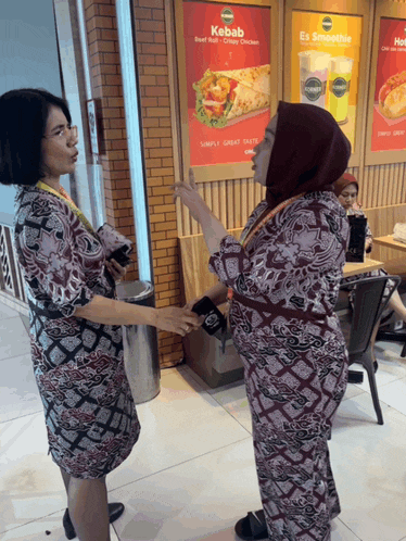two women standing in front of a kebab sign