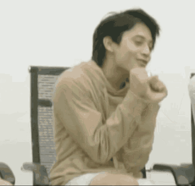 a young man is sitting in a chair with his hands on his chin and making a funny face .