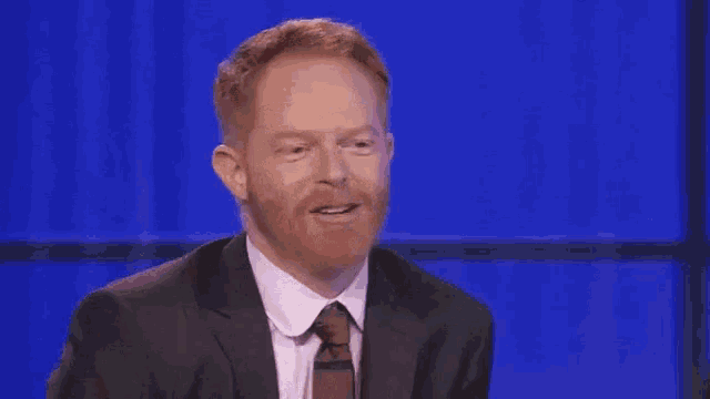 a man with a red beard is wearing a suit and tie and blowing a kiss .