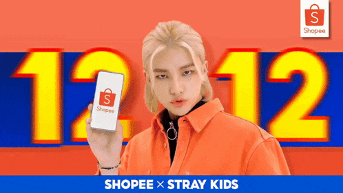 a man is holding a shopee phone in front of a sign that says 12:12