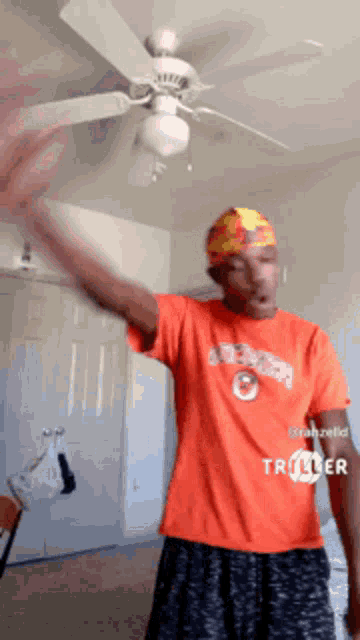 a man wearing an orange shirt with the number 8 on it is standing in front of a ceiling fan