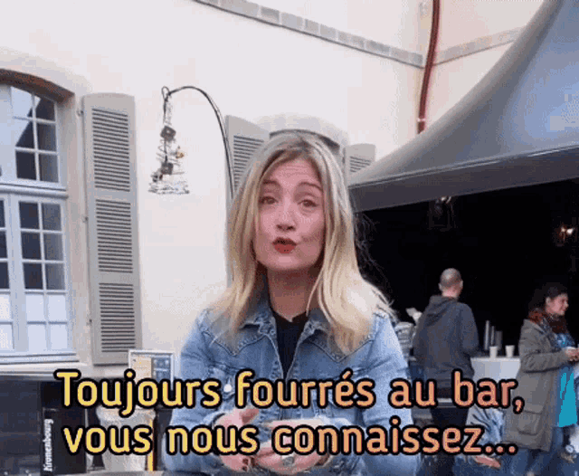 a woman in a denim jacket says " toujours fourres au bar vous nous connaissez "