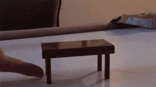 a person 's finger is reaching for a small wooden table on a table