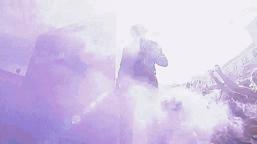 a man is standing in a crowd of people surrounded by purple smoke