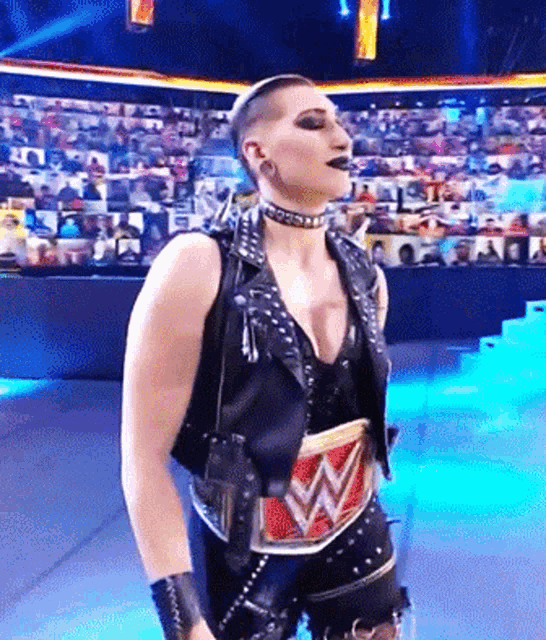 a woman in a leather vest is standing on a stage with a w belt around her waist