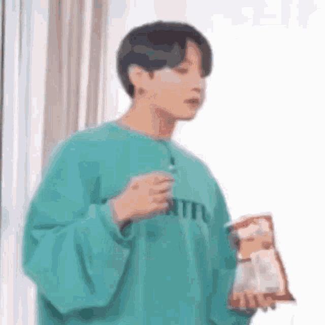 a young man in a blue sweater is holding a bag of chips .