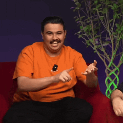 a man in an orange shirt is sitting on a red couch and smiling