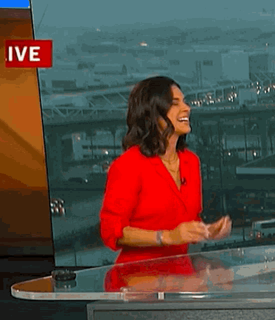 a woman in a red shirt is standing in front of a live screen