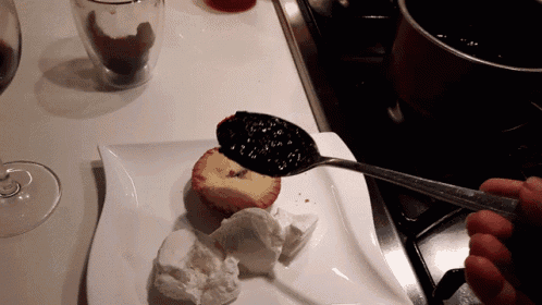 a spoon is being used to spread jam on a cupcake on a white plate