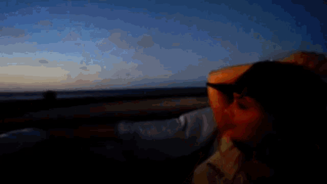 a woman wearing a hat and sunglasses looks out a car window at the ocean