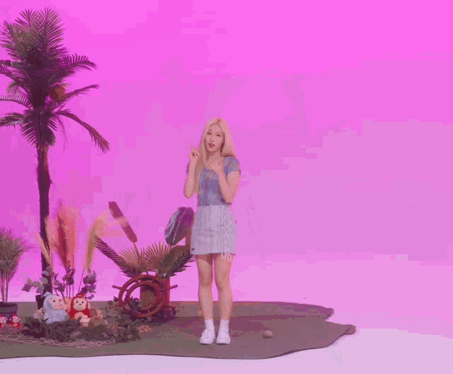 a woman standing in front of a pink background with stuffed animals and palm trees